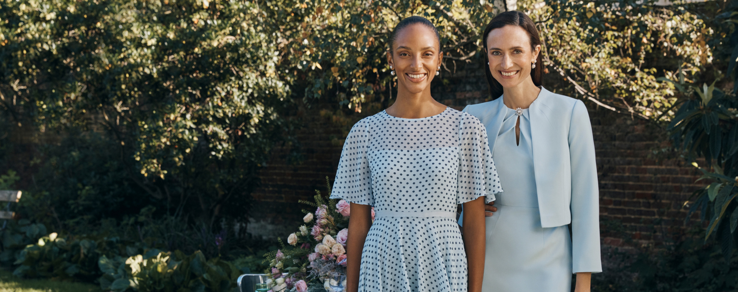 Image of two models outside at a wedding wearing occasion outfits.