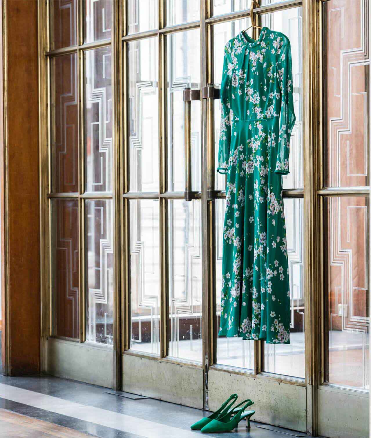 A green floral silk dress hangs on large brass and glass doors.