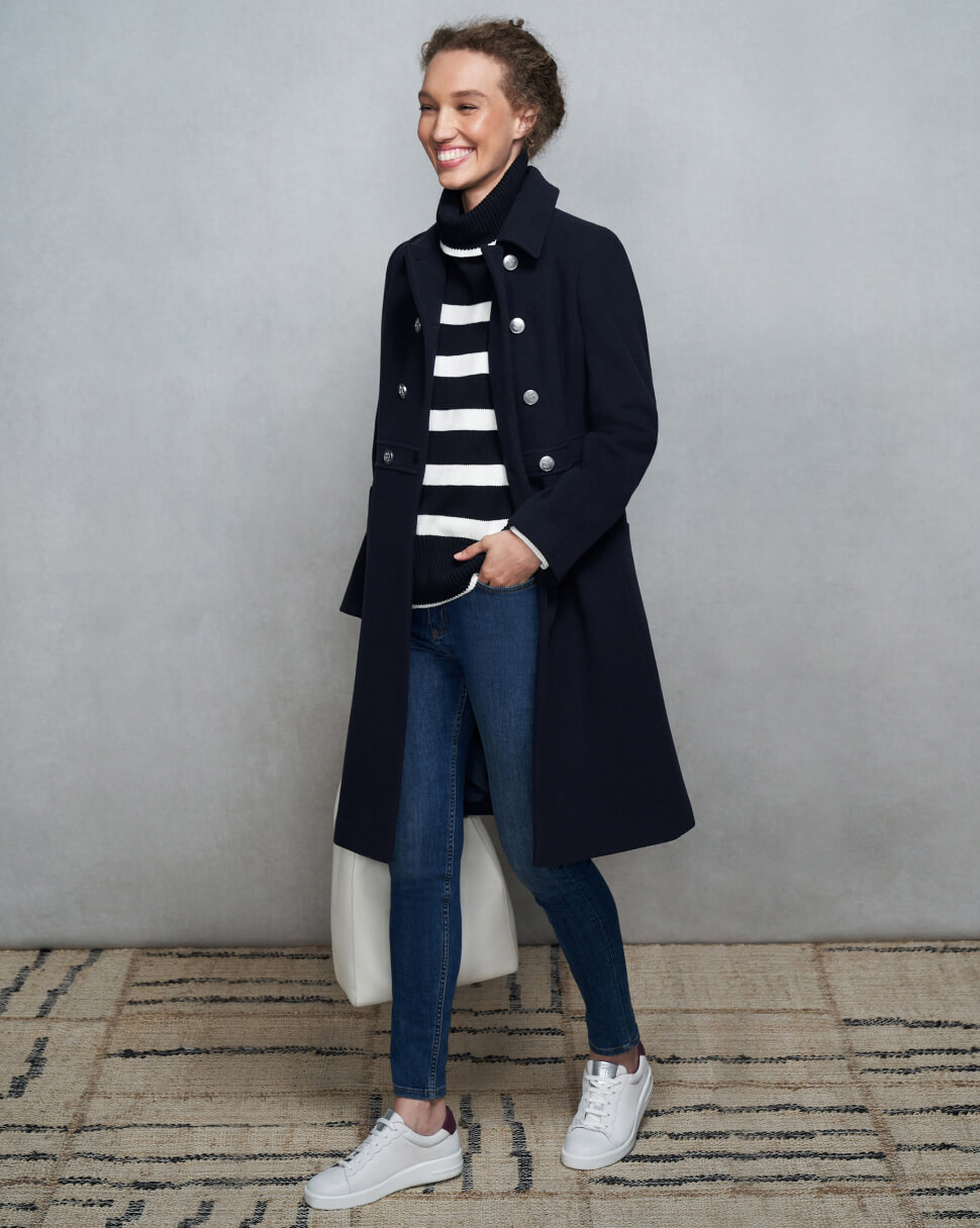 Model photographed against a canvas background wearing a Hobbs navy coat, striped jumper and jeans.