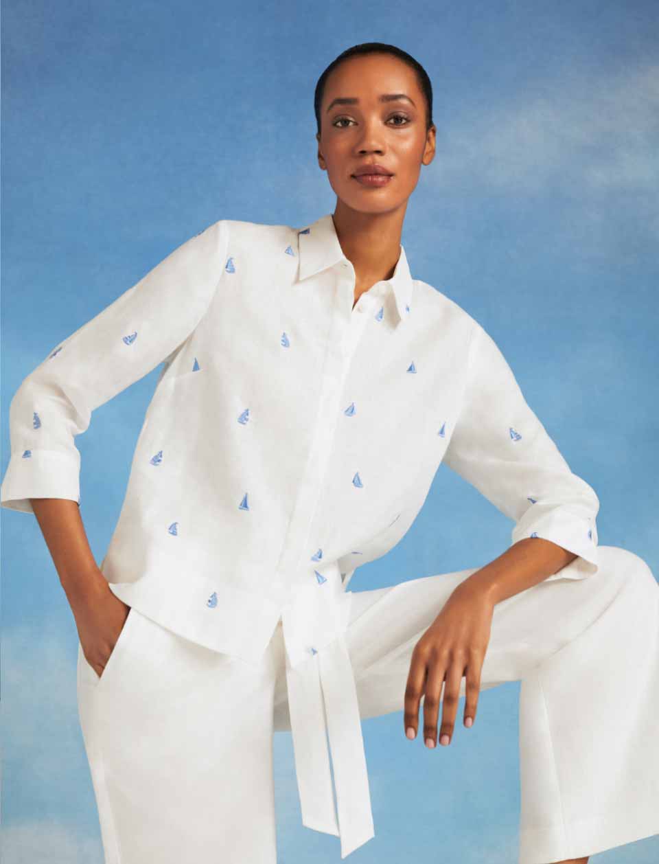 Close-up image of model pictured in front of a sky blue background wearing a white linen shirt.