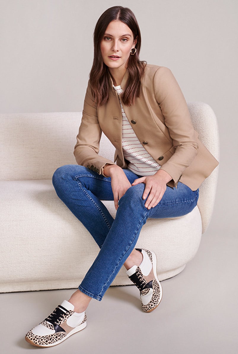 Model sits on a cream sofa wearing a military style jacket, jeans and leopard trainers.