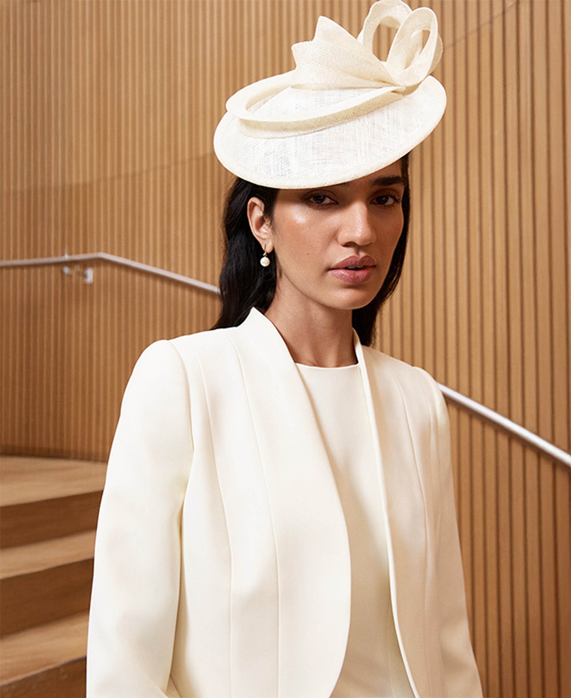 A woman wearing a butter yellow fascinator, dress and jacket.