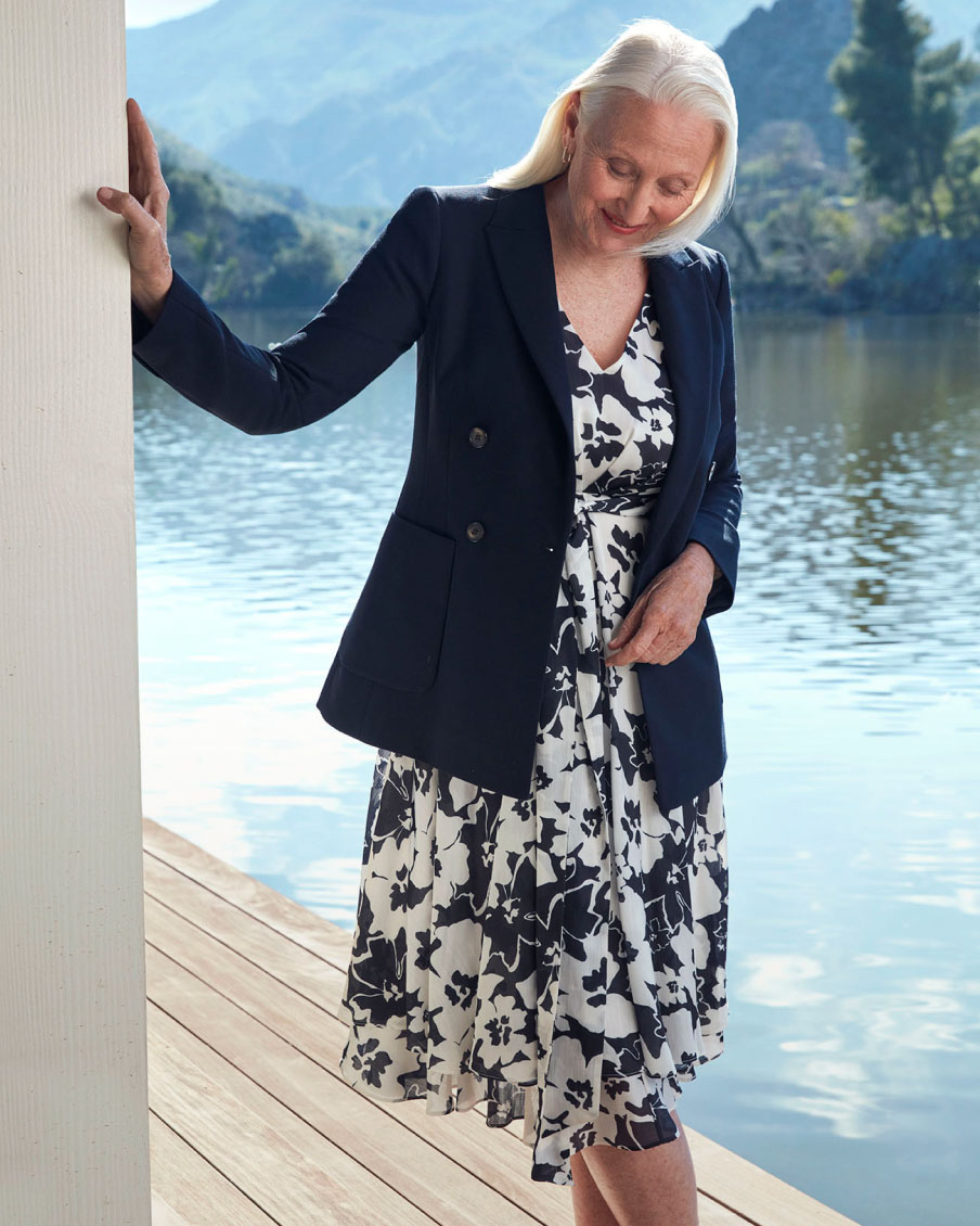 Image of a model pictured in front of a lake wearing a floral summer dress and a blazer jacket.