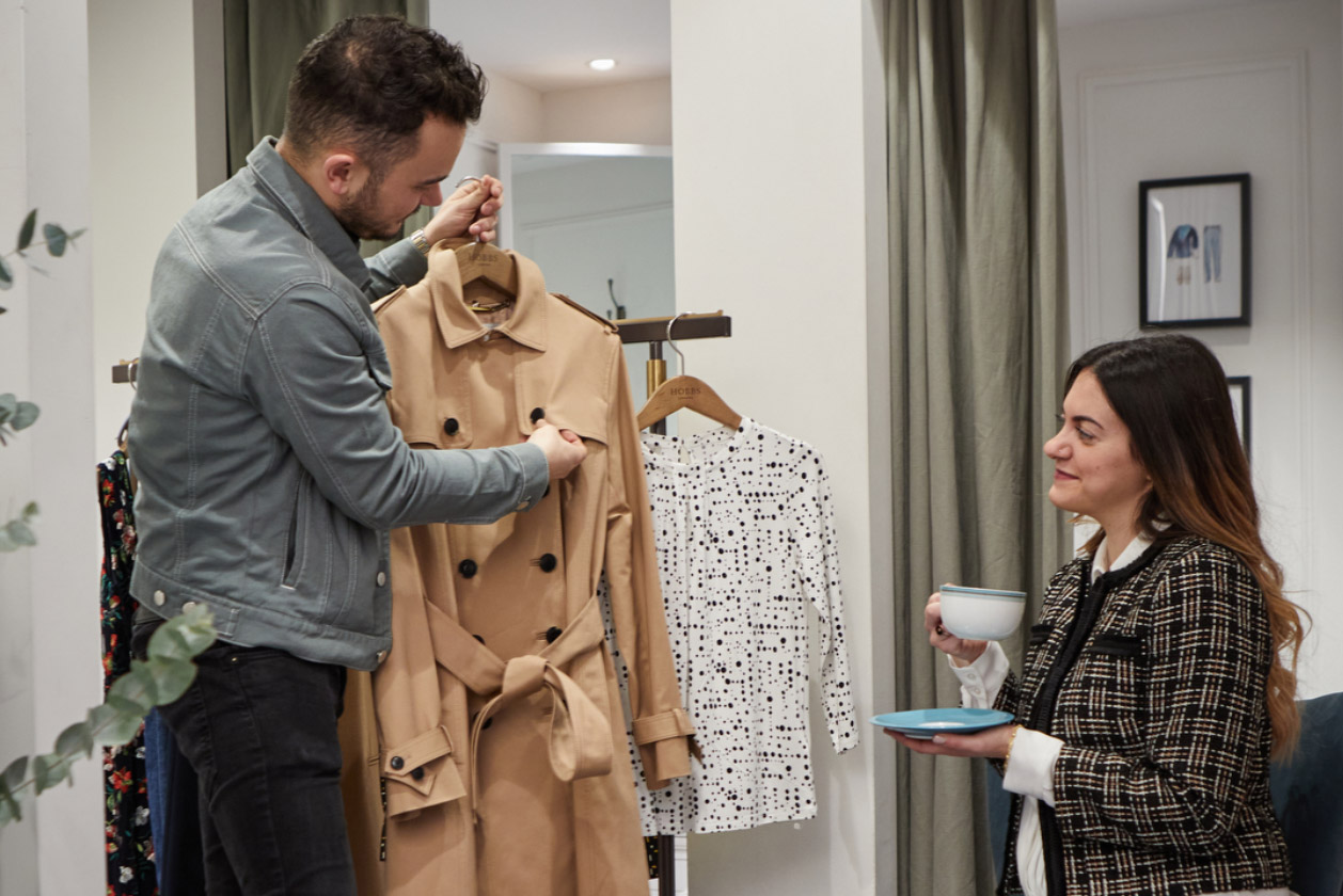 A clothing rail in a Hobbs store, featuring a pink blazer, a white dotted top underneath and the strap of a red leather crossbody bag on a hanger and other garments in the background.