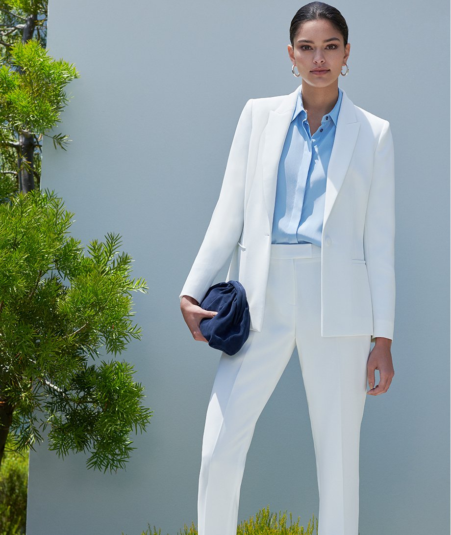 Women's trouser suit in white worn with light blue shirt and dark navy clutch by Hobbs.