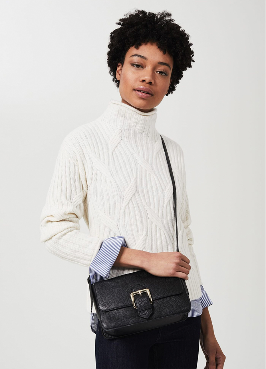 Image of model wearing a cream cable neck sweater layered over a pinstripe shirt. 