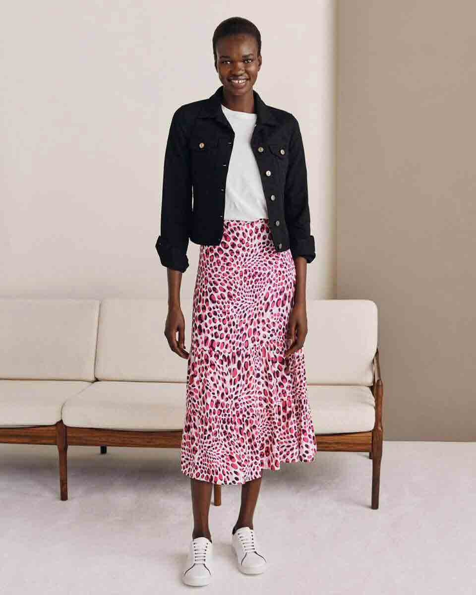 Hobbs model stands in front of a sofa wearing an abstract leopard print skirt with a t-shirt and denim jacket.