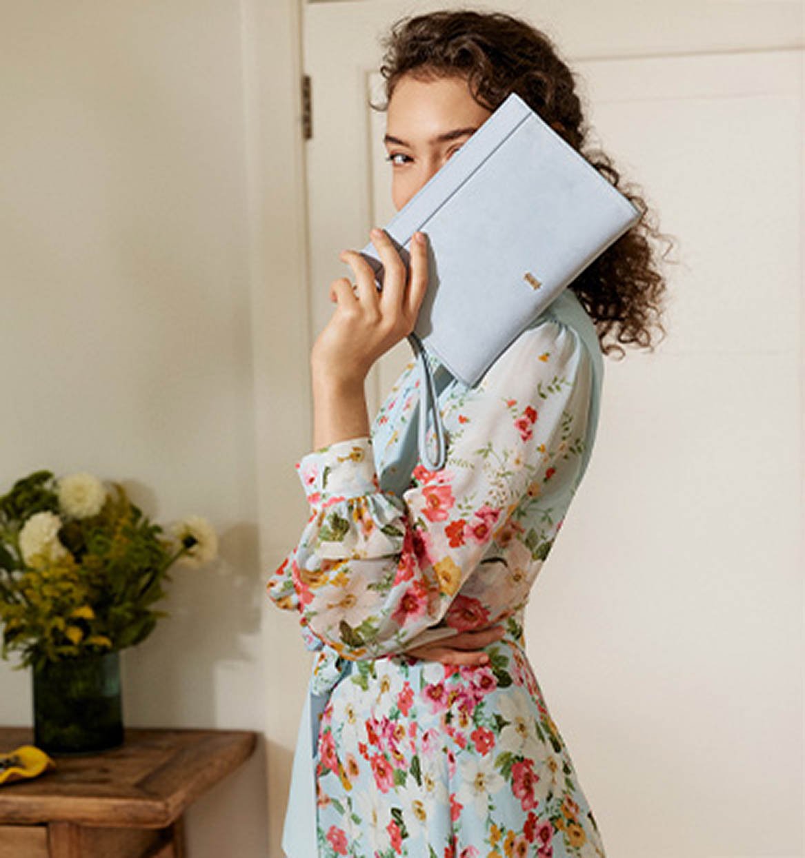 A woman wearing a Hobbs occasion dress and colour-matched clutch bag.