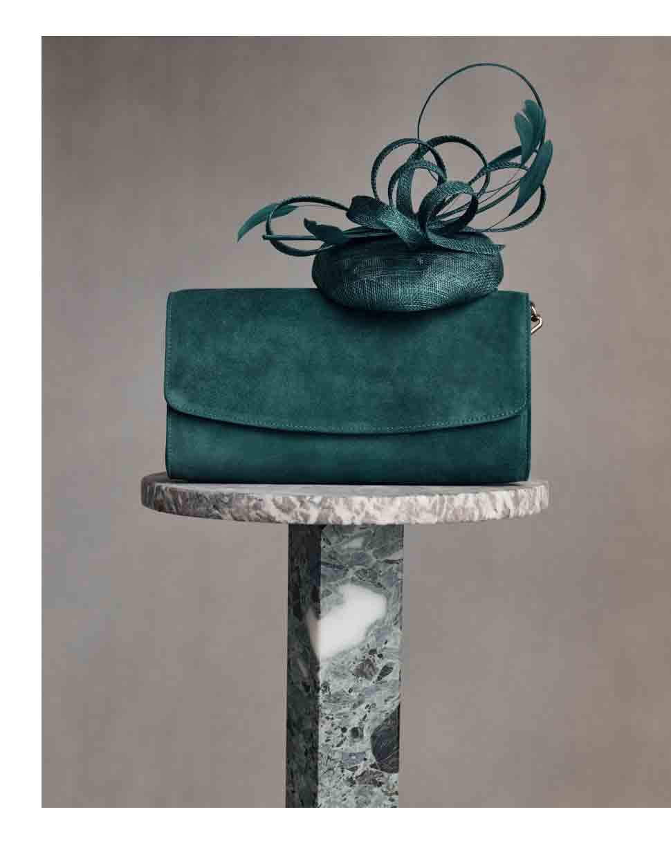A green suede clutch bag and matching fascinator sit atop a marble plinth