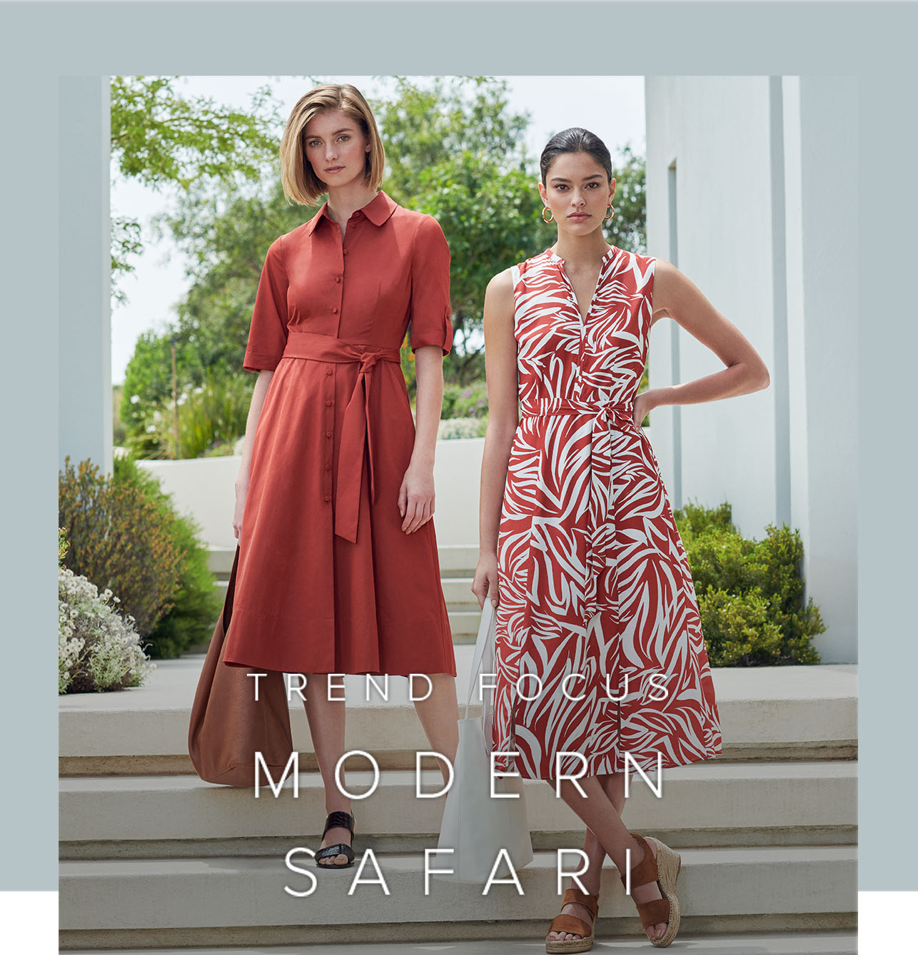Two women pose against a modernist architectural background. One wears a brown knee-length shirt dress and the other a rust brown and wite patterned midi length dress.