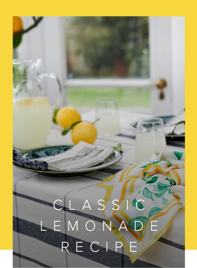 A jug of homemade lemonade, bowl of fresh lemons and a silk scarf sit atop a table.