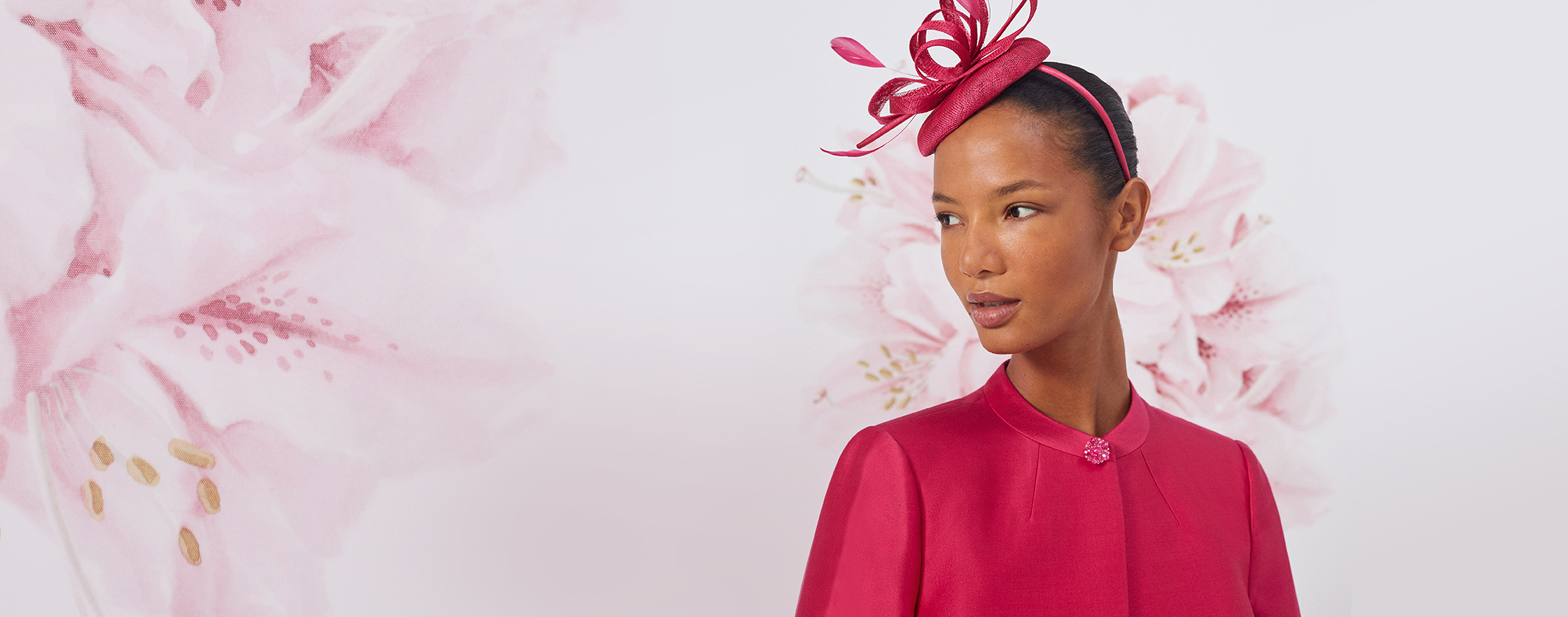 Close up image of model against a floral painted background wearing a Hobbs fuschia pink jacket and fascinator.