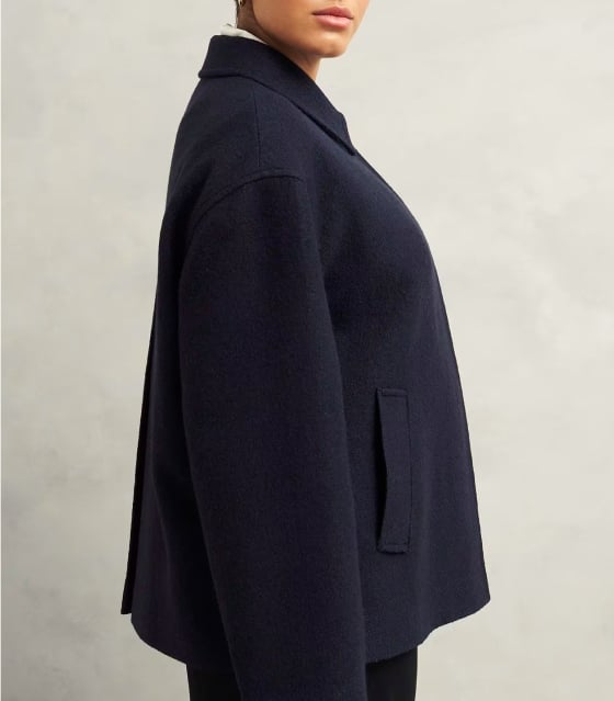 A gallery of four images including one image of a model wearing a navy coat, and three smaller images displaying details of the coat.