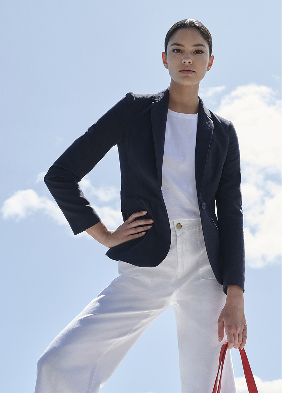 Women’s blazer in black paired with a white top, white wide leg trousers and a red bag from Hobbs.