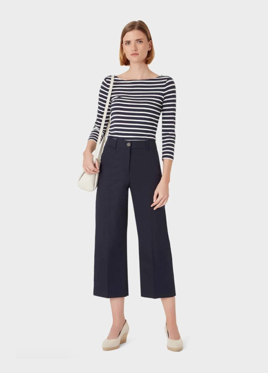 Mid-sleeve top with black and white stripes paired with black wide trousers for women, wedge espadrilles in nude and a white crossbody bag.