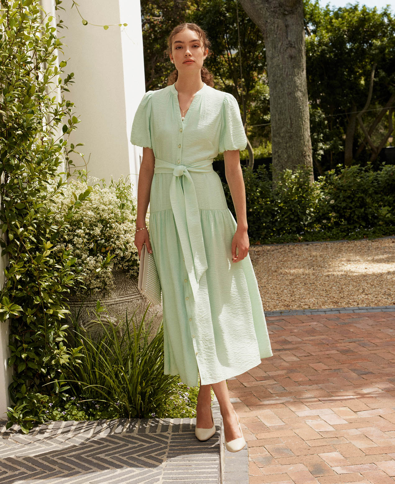 A woman wearing a mint, tie-waist, occasion dress.