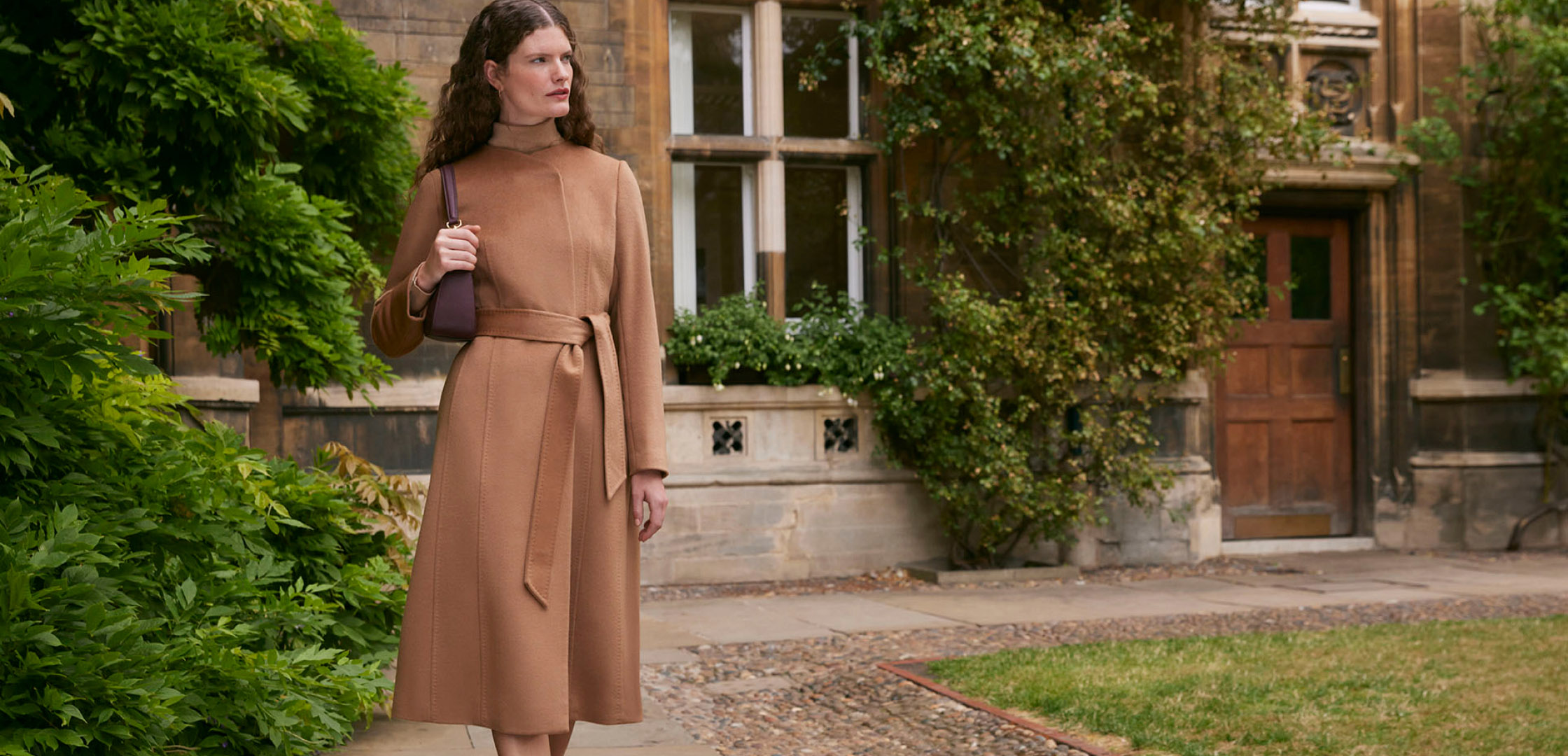 Model photographed walking by a historic building wearing a camel wool coat.