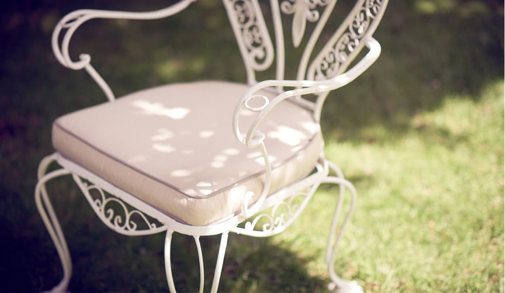 A white wrought iron chair with a pale pink cushion.