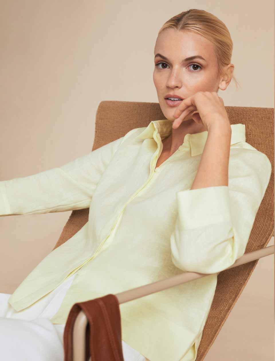 Close-up image of model photographed in front of a beige background wearing a yellow linen shirt.
