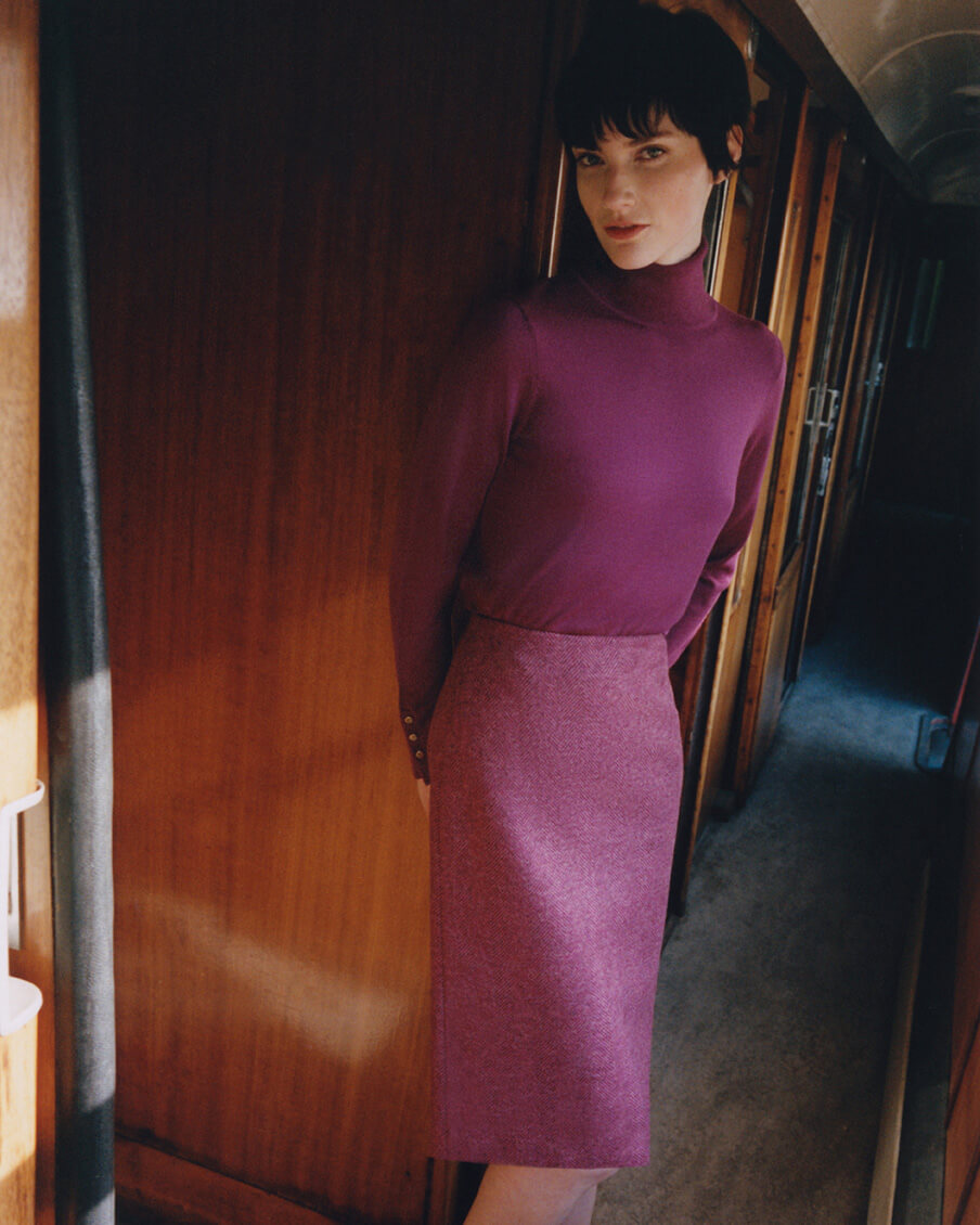 Hobbs model stands inside a train carriage wearing a tweed pencil skirt and roll neck jumper.