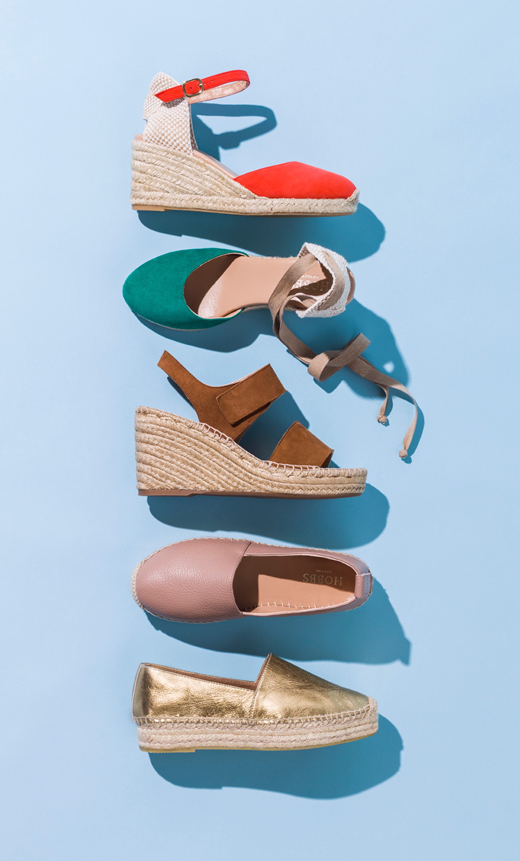 A variety of espadrille sandals lie, displayed on a pale blue background