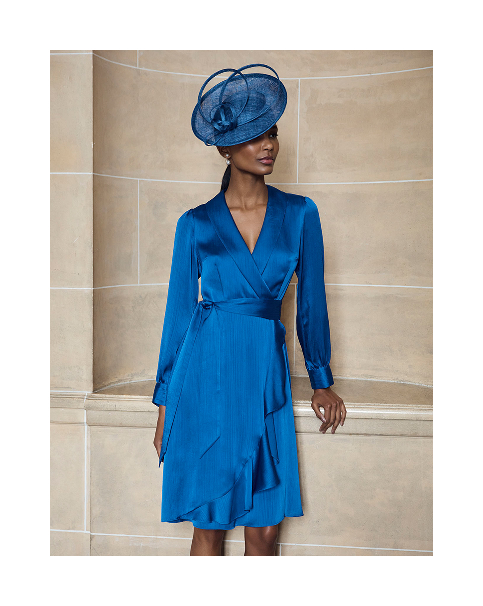 Hobbs model wears a blue satin wrap dress and matching fascinator.