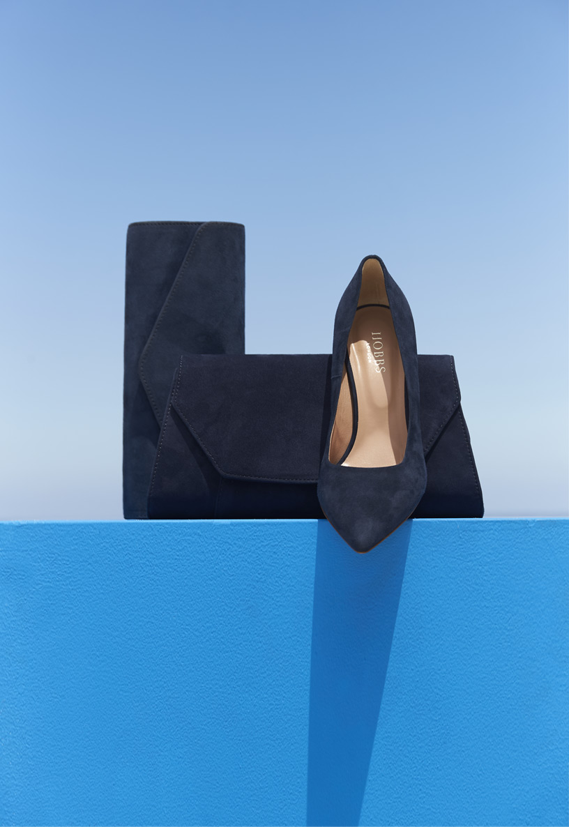 Grouping of matching navy blue accessories including two navy suede clutch bags alongside a classic navy pointed court shoe.