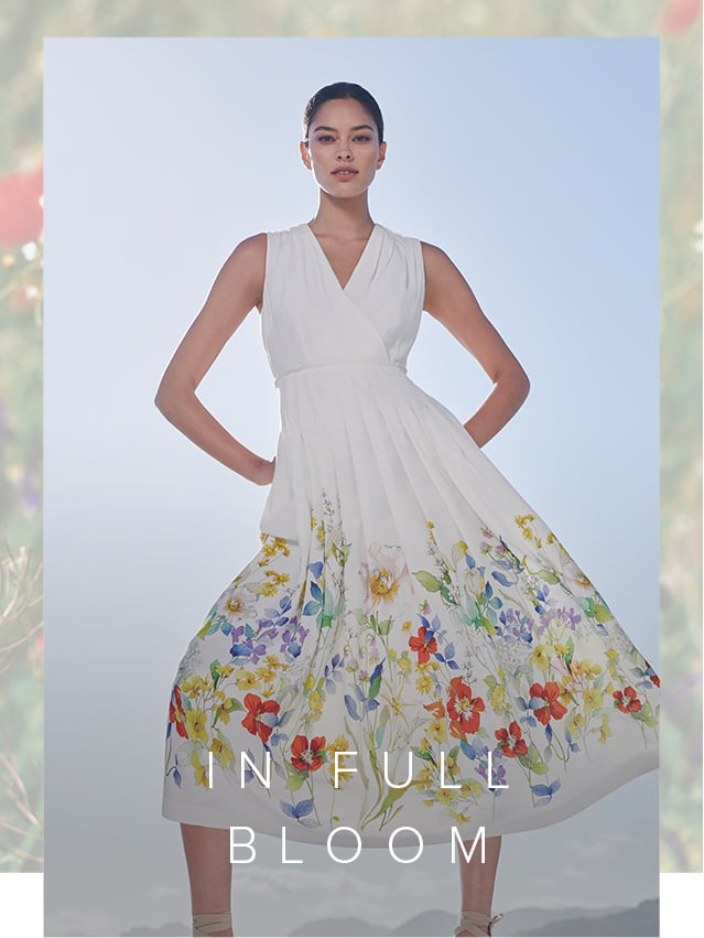 Woman poses in an elegant white midi dress with a floral motif along the bottom edge