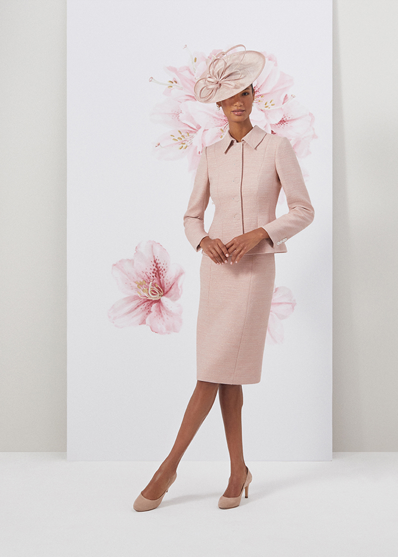 Image of model standing in front of a floral painted background wearing a matching oyster pink jacket and dress two piece outfit.
