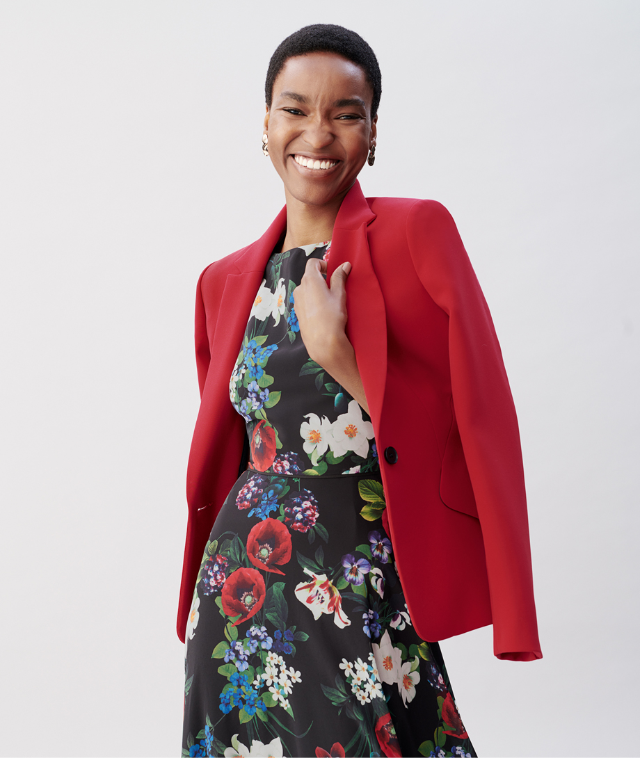 Hobbs model wearing a red blazer draped over a floral midi dress.