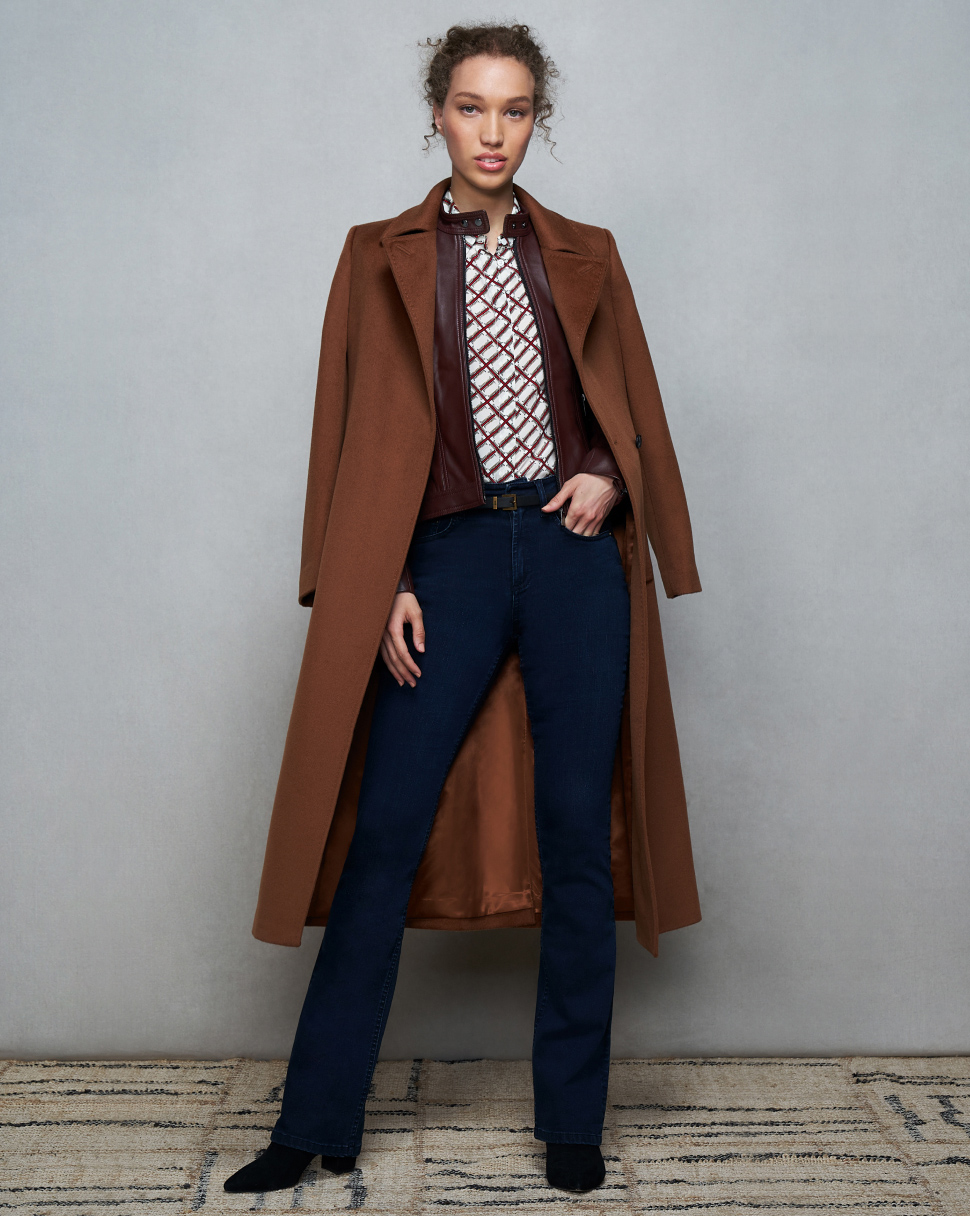 Model photographed against a canvas background wearing Hobbs tan coatover a brown leather biker jacket.
