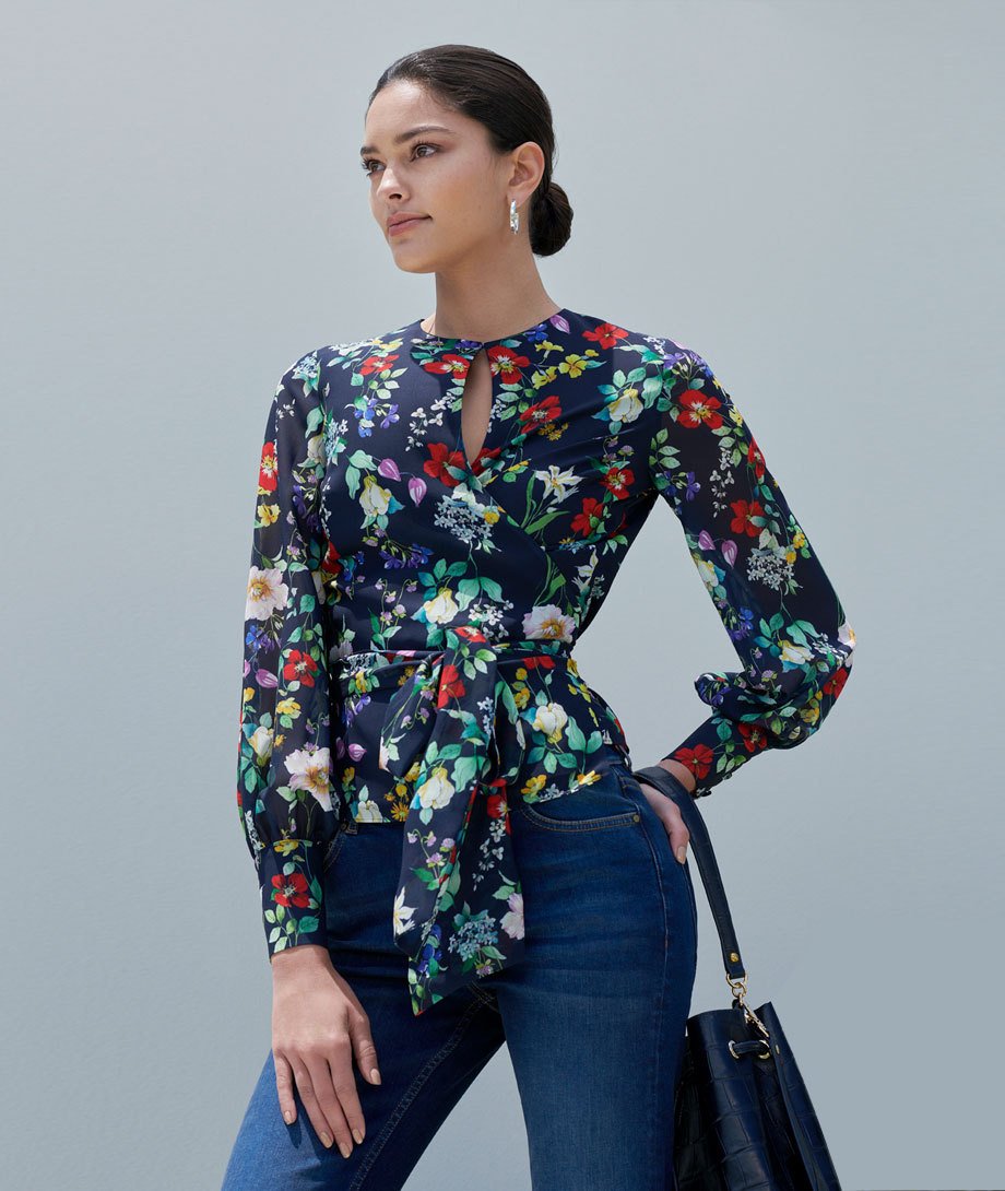 Floral wrap blouse with waist tie detail, worn with indigo blue jeans and a dark blue leather bucket bag, by Hobbs.