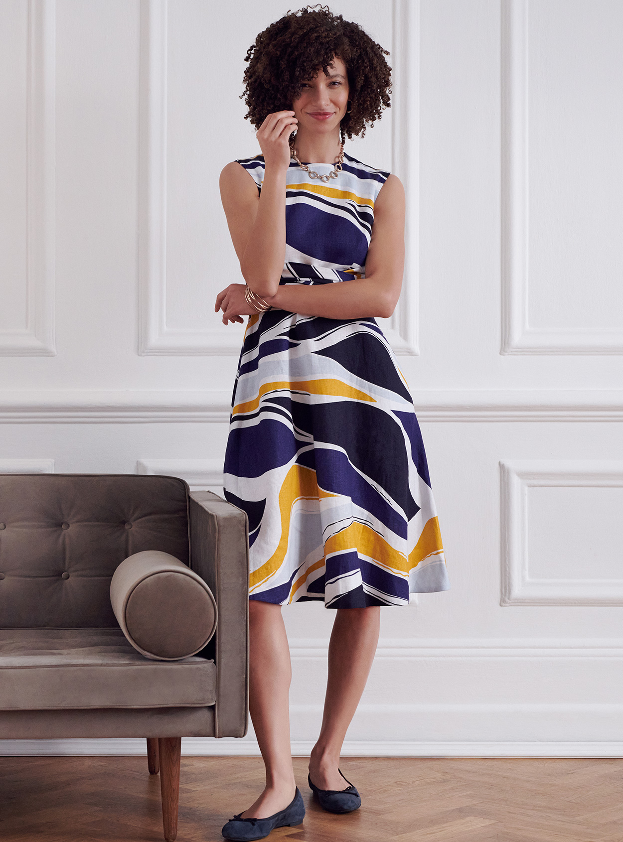 Photographed next to a contemporary armchair, model wears a printed fit and flare linen dress.