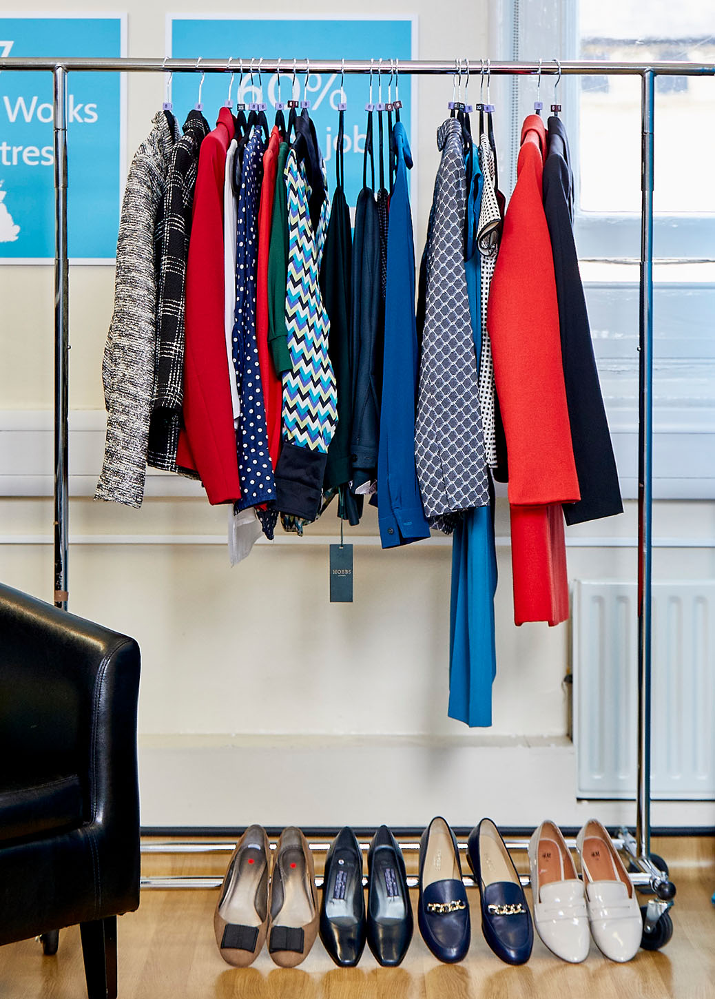 Rail Of Blue And Red Workwear With Complimentary Shoes Lined Up Below.