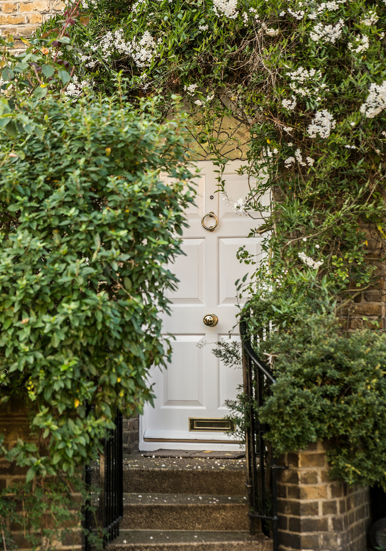 A flight of brick stairs lead to a white front surrunded by greenery and white flowers