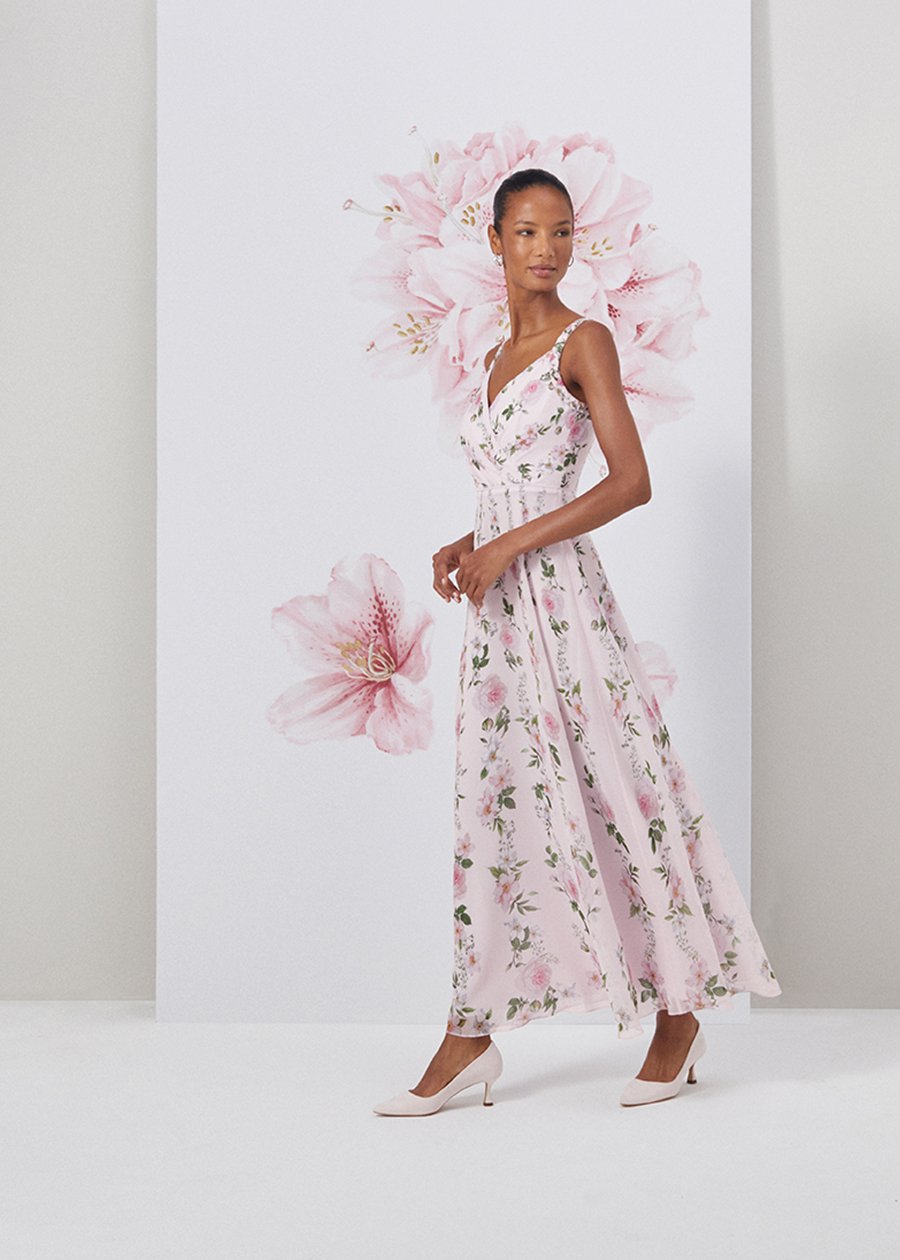 Image of model standing in front of a floral painted background wearing a floral print maxi dress.