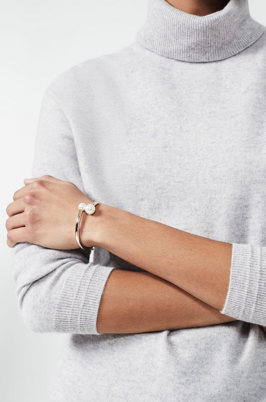 Model photographed wearing a grey jumper with a gold pearl embellished cuff.