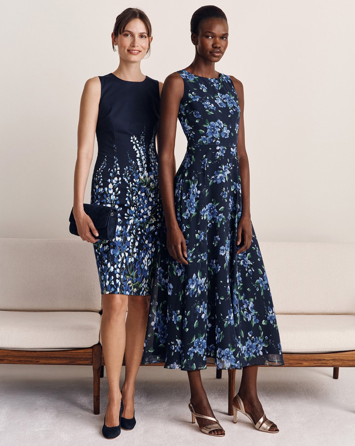 Hobbs models stand in front of a cream sofa wearing floral occasion dresses.