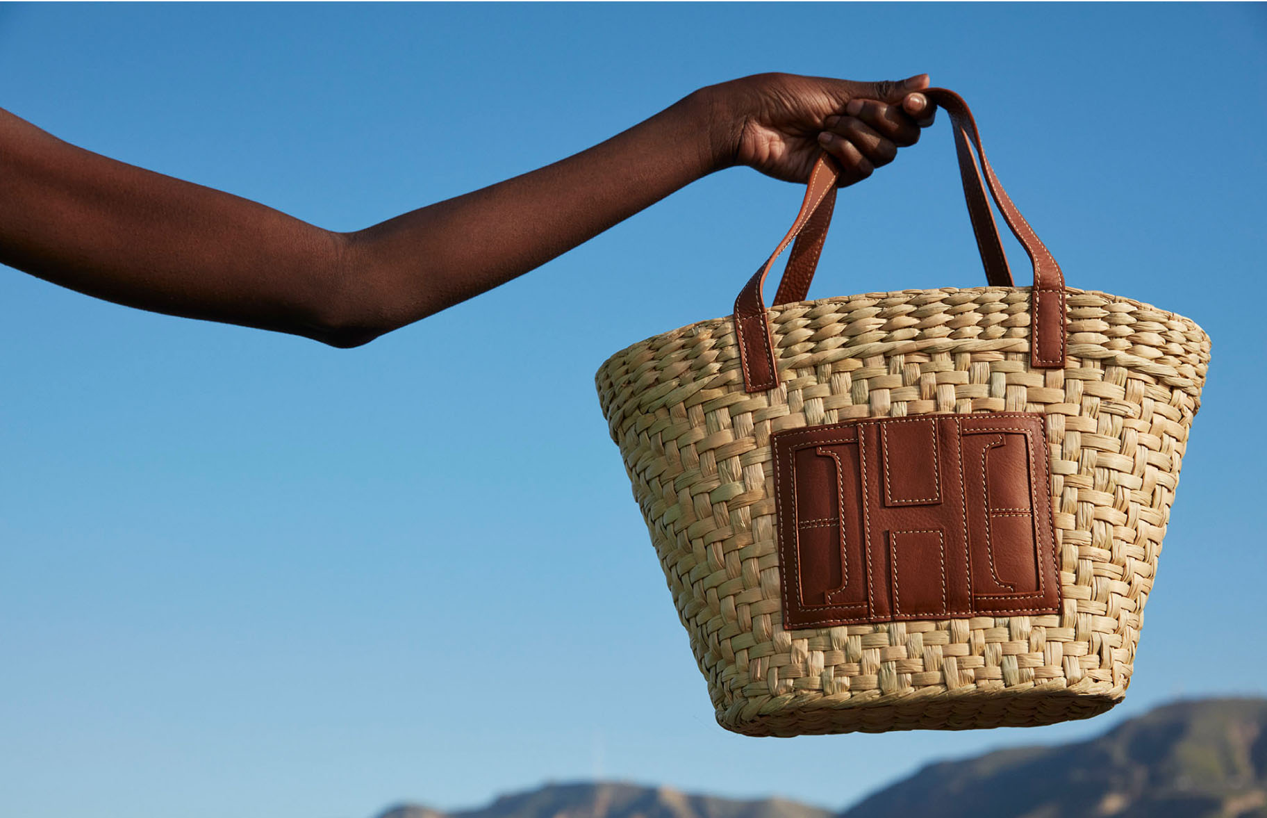 Image of a model's hand holding a woven tote handbag.