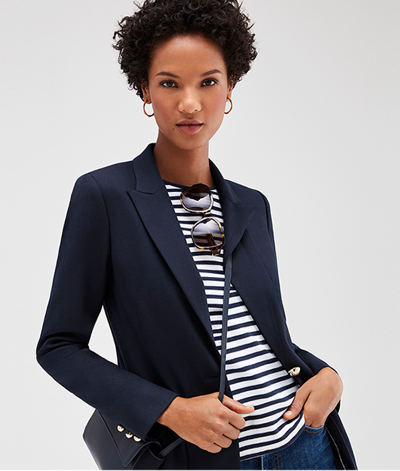 Model wears a navy blazer, striped top, jeans with a navy blue cross body bag