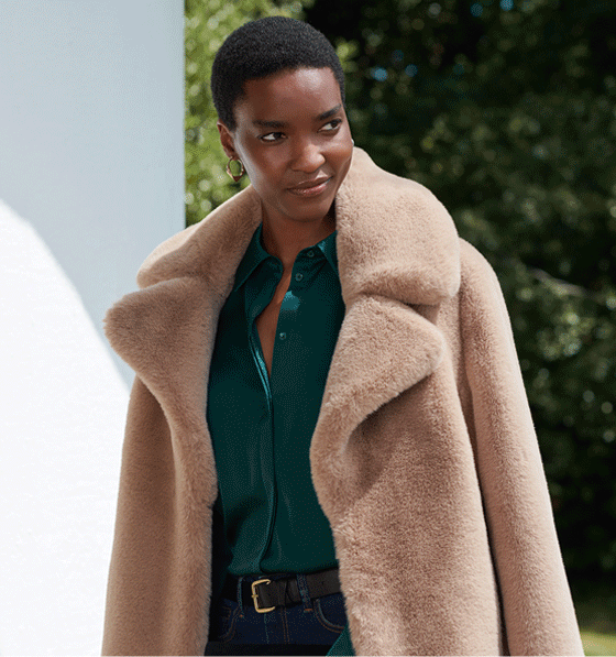 Model photographed outdoors wearing a beige faux fur coat over her shoulders.