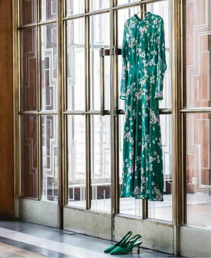 A green floral silk dress hangs on large brass and glass doors.