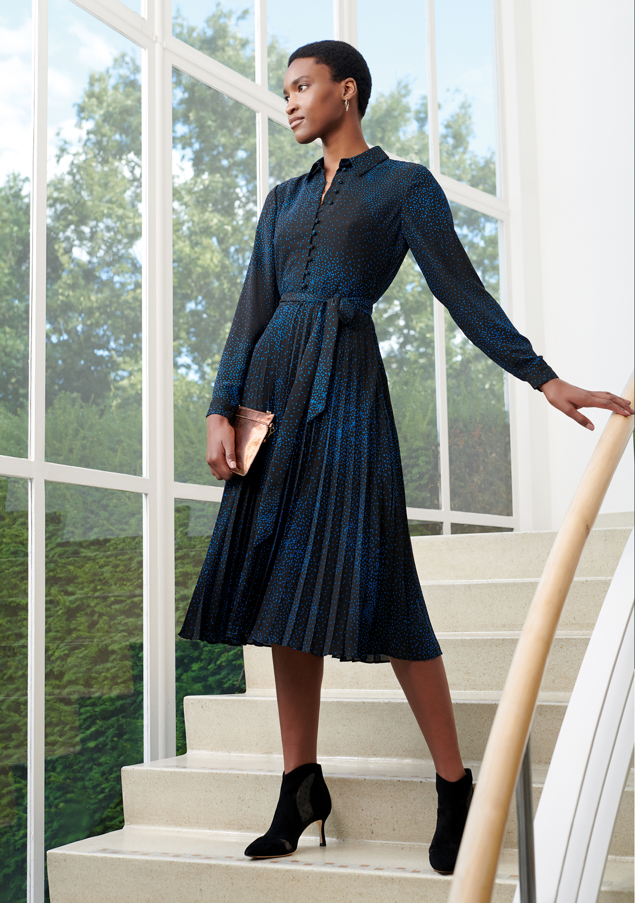 Hobbs model wearing a long sleeve shirt dress in blue and black, styled with a metallic pink clutch and heeled ankle boots in black.