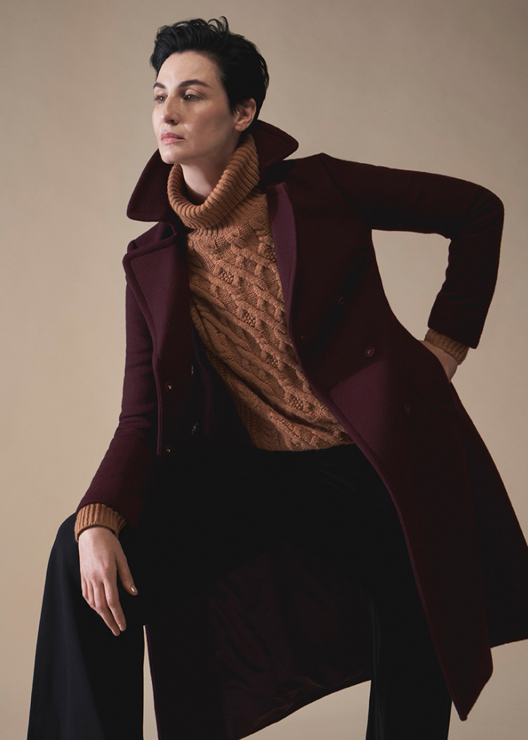 Model Erin O'Connor photographed leaning, wearing a Hobbs tailored wool wrap coat over a cable knit jumper.