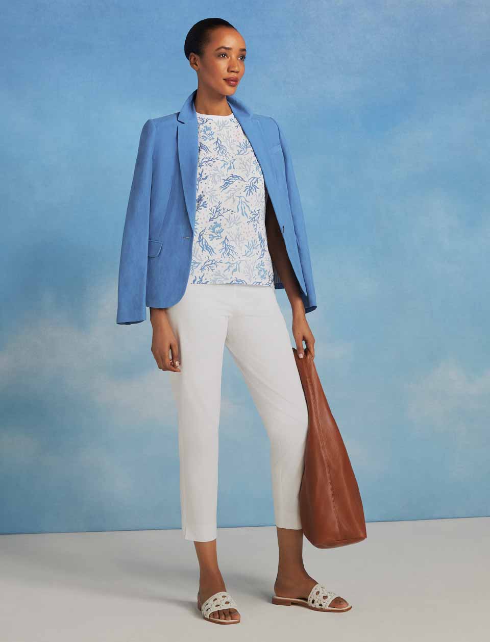 Model pictured in front of a sky blue background wearing a blazer, t-shirt and jeans. 
