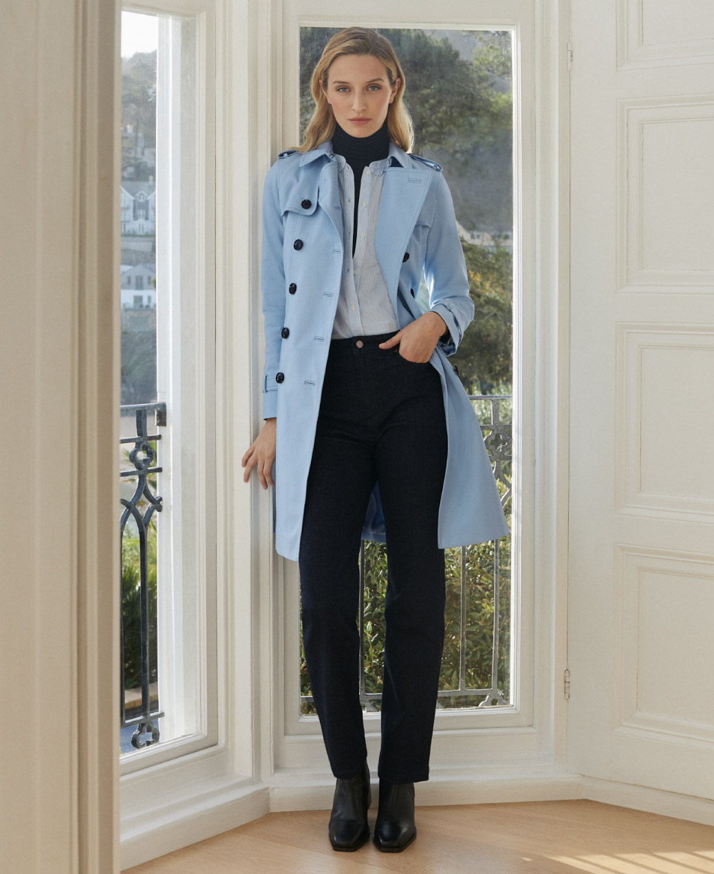 Hobbs model standing by a window wearing a pale blue trench coat