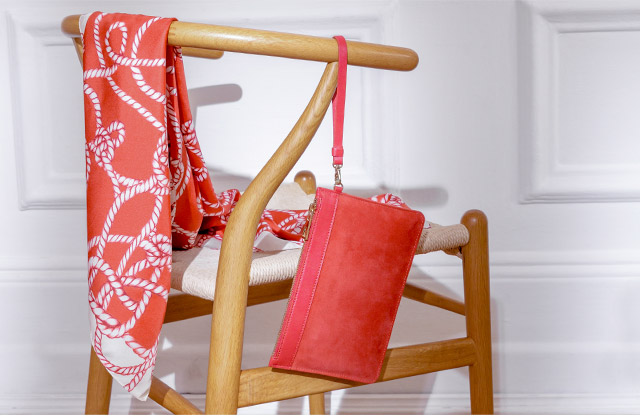 Image of a chair, casually displaying a red rope print scarf and red clutch bag