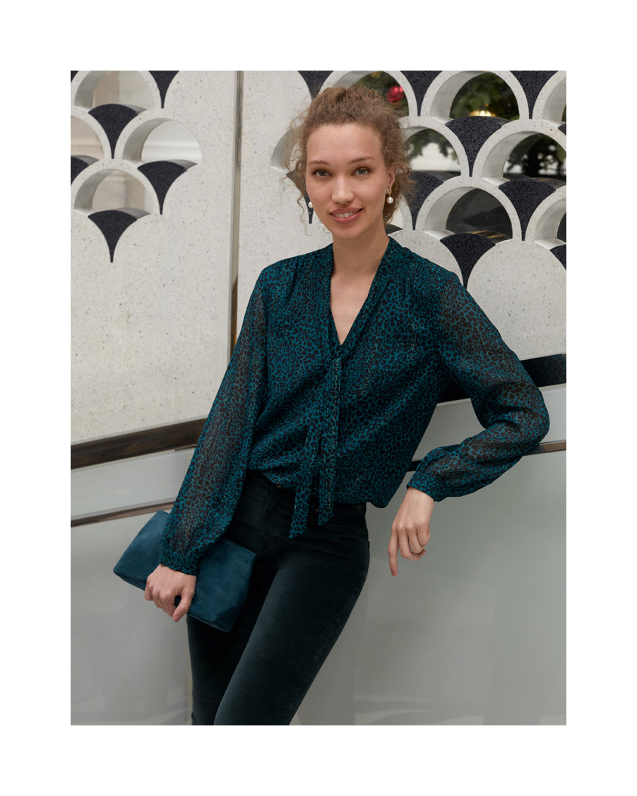 Hobbs model wears an animal print blouse with velvet jeans and a clutch bag.