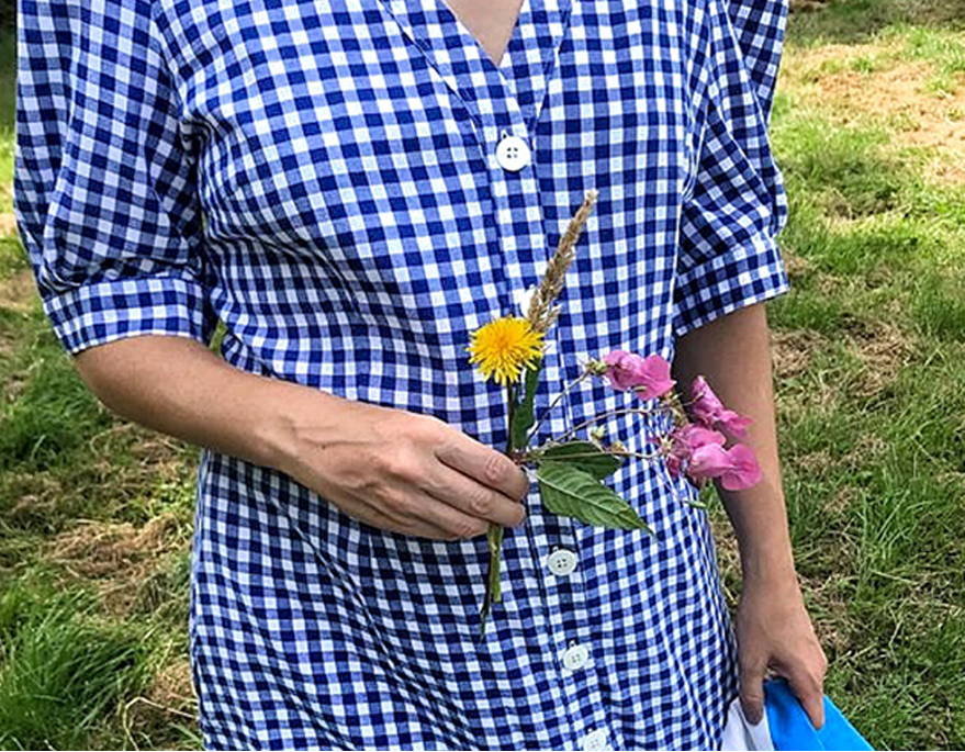 A close up image of Maddy Moxham, Brand Stylist at Hobbs wearing a gingham button down dress in blue and white while holding some flowers.