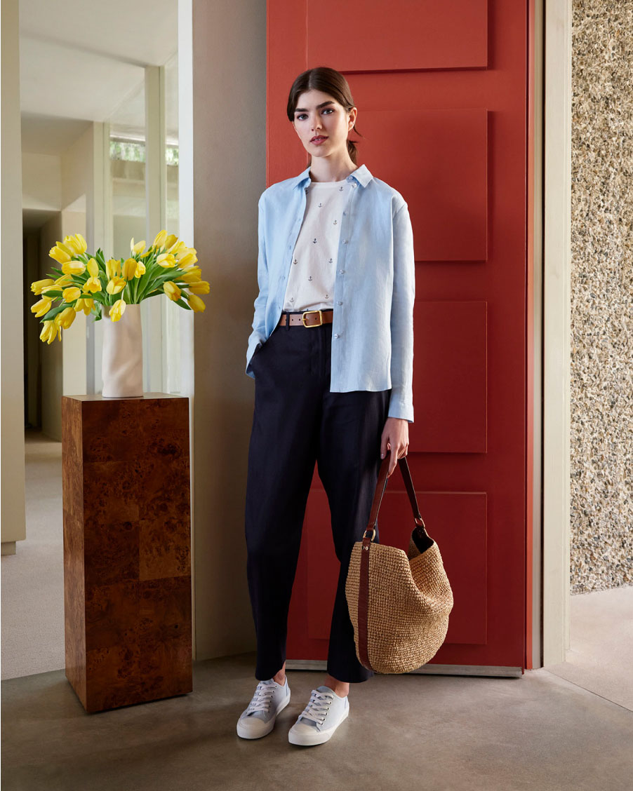 Image of model pictured in front of a door wearing a linen shirt over a t-shirt with chino trousers.